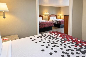 A hotel room with two beds, each with a patterned bedspread, a bedside table with a lamp, and a carpeted floor.