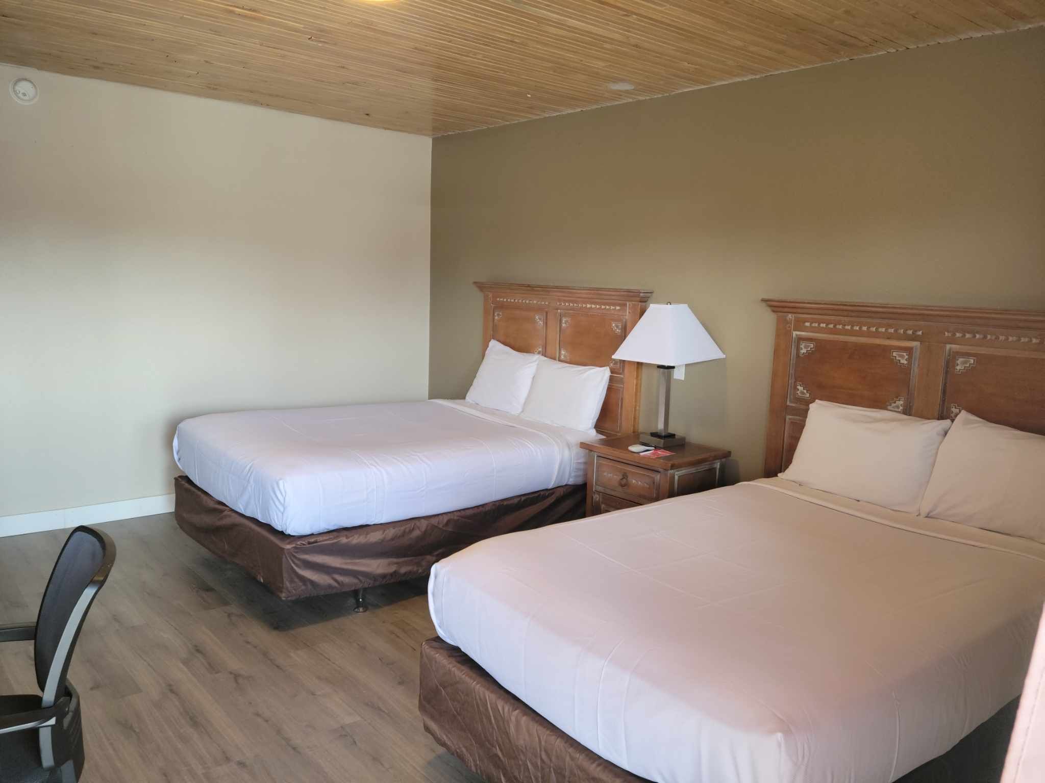 Ein Hotelzimmer mit zwei Betten, Holz-Kopfteilen, einem Nachttisch mit Lampe und einem Sessel.