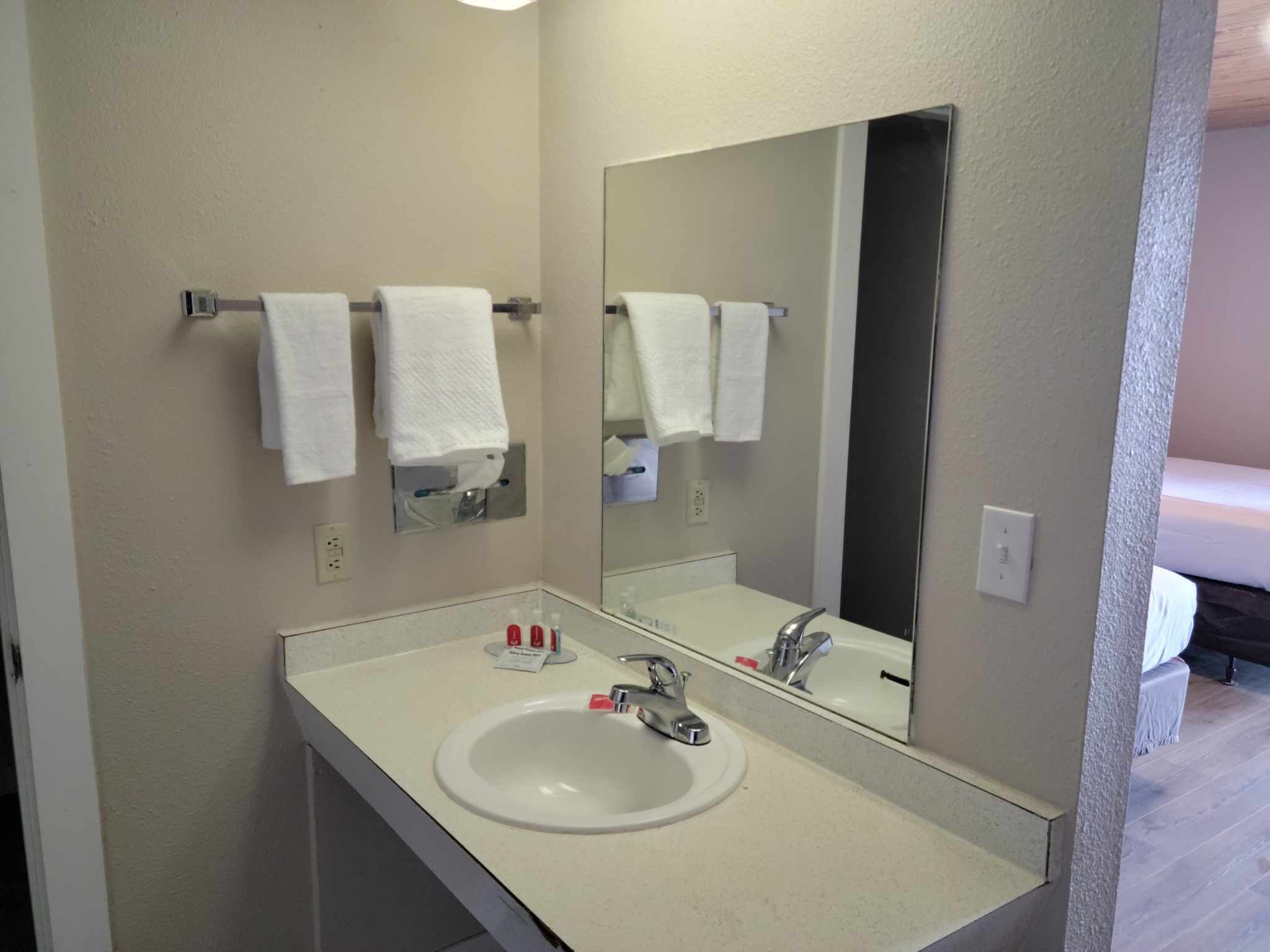 Une salle de bain avec un lavabo blanc, un miroir et deux serviettes suspendues à un porte-serviettes.