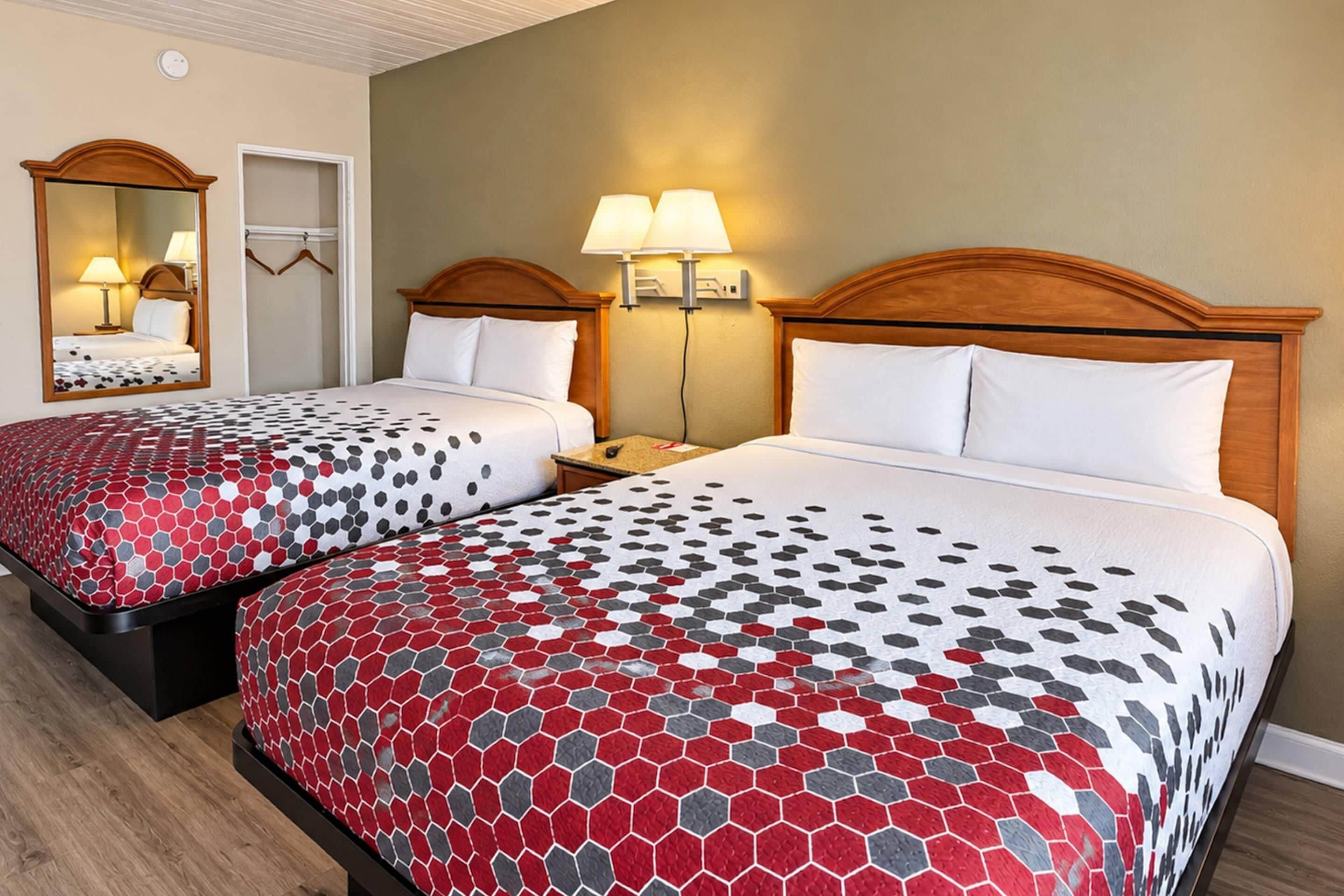 Een hotelkamer met twee bedden, elk met een houten hoofdbord, nachtkastje en een lamp aan de muur.