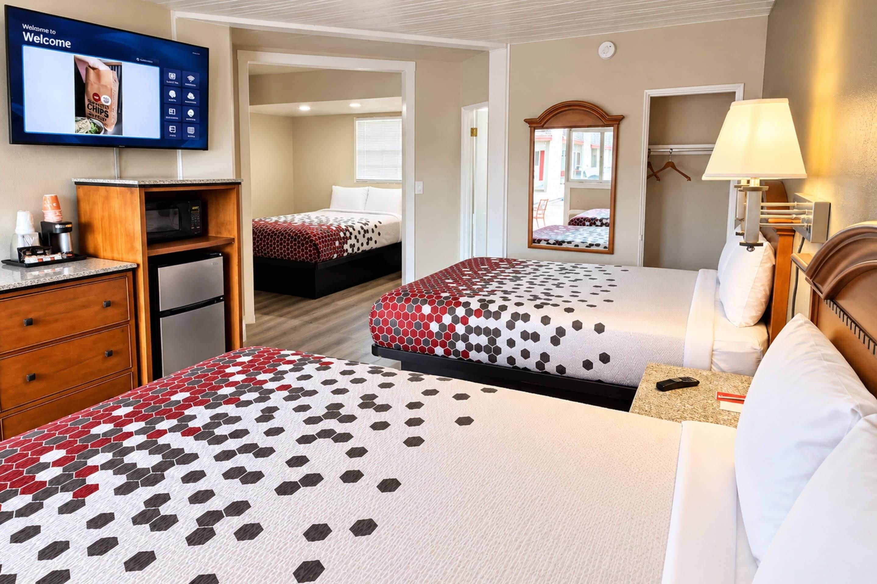 Habitación de hotel con dos camas, televisor, escritorio y cafetera, y un espejo.