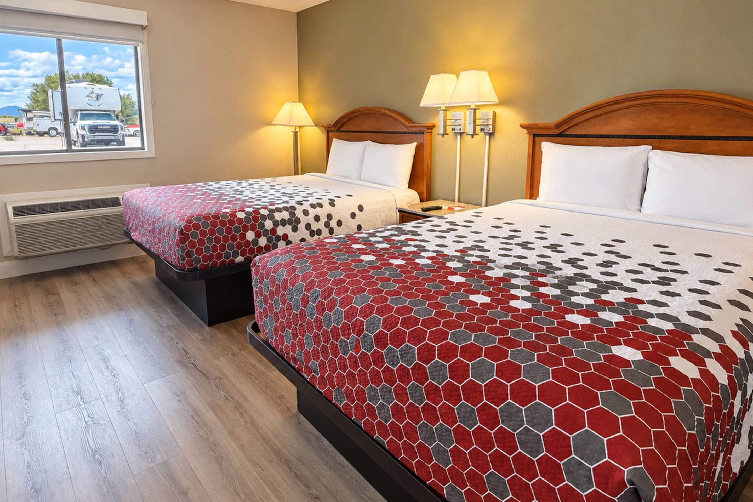 Habitación de hotel con dos camas, cada una con una colcha estampada, lámparas de noche y una ventana con vista a vehículos estacionados.
