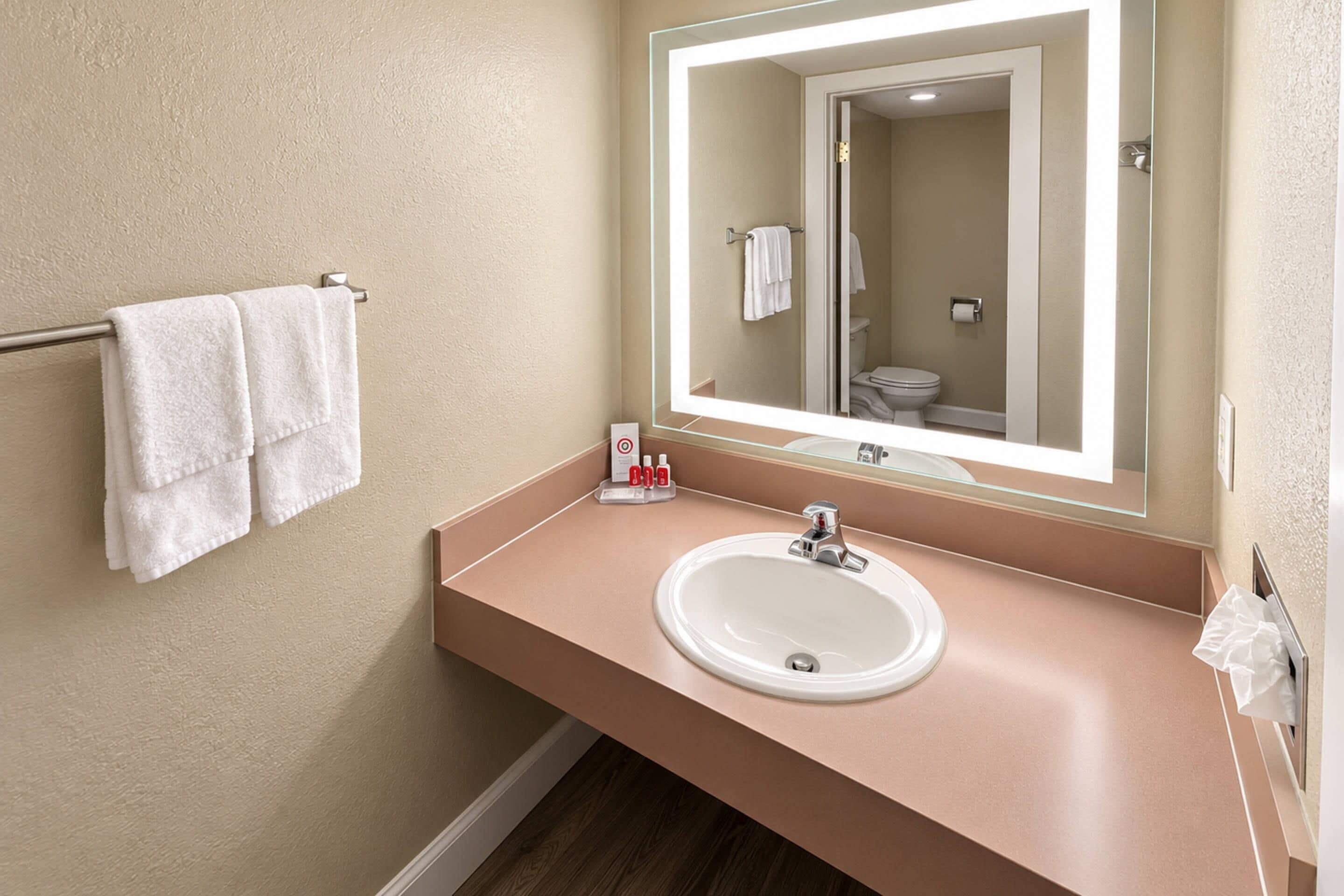 A bathroom with a beige wall, a white sink, a mirror, and a towel rack with two towels.