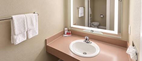 A bathroom with a beige wall, a white sink, a mirror, and a towel rack with two towels.