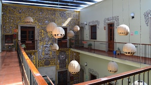 A multi-level atrium with patterned walls, hanging lamps, and a wooden railing. - Hotel La Rotonda (Guadalajara)