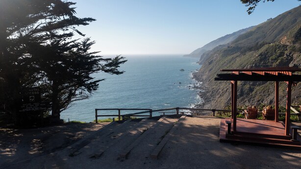 A coastal viewpoint with a wooden gazebo and a sign indicating a nature trail access.