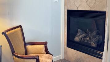 A corner room with a fireplace, a wooden chair, and a carpeted floor.