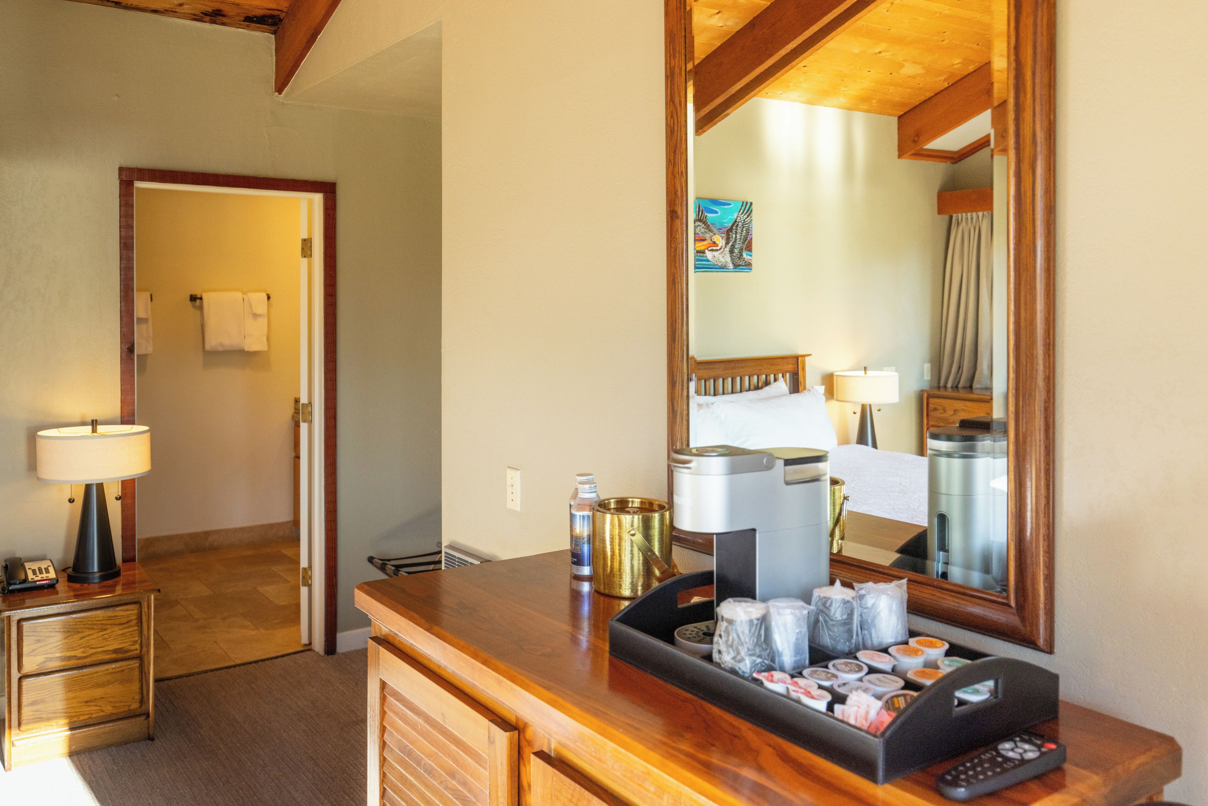 A hotel room with a wooden desk, a lamp, a coffee maker, and a tray of toiletries.