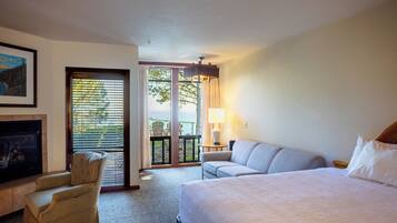 A hotel room with a bed, a sofa, a chair, a fireplace, and a balcony with a view.