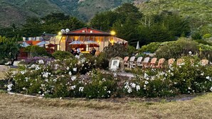 A restaurant with outdoor seating, surrounded by a garden with white flowers and a mountainous backdrop.