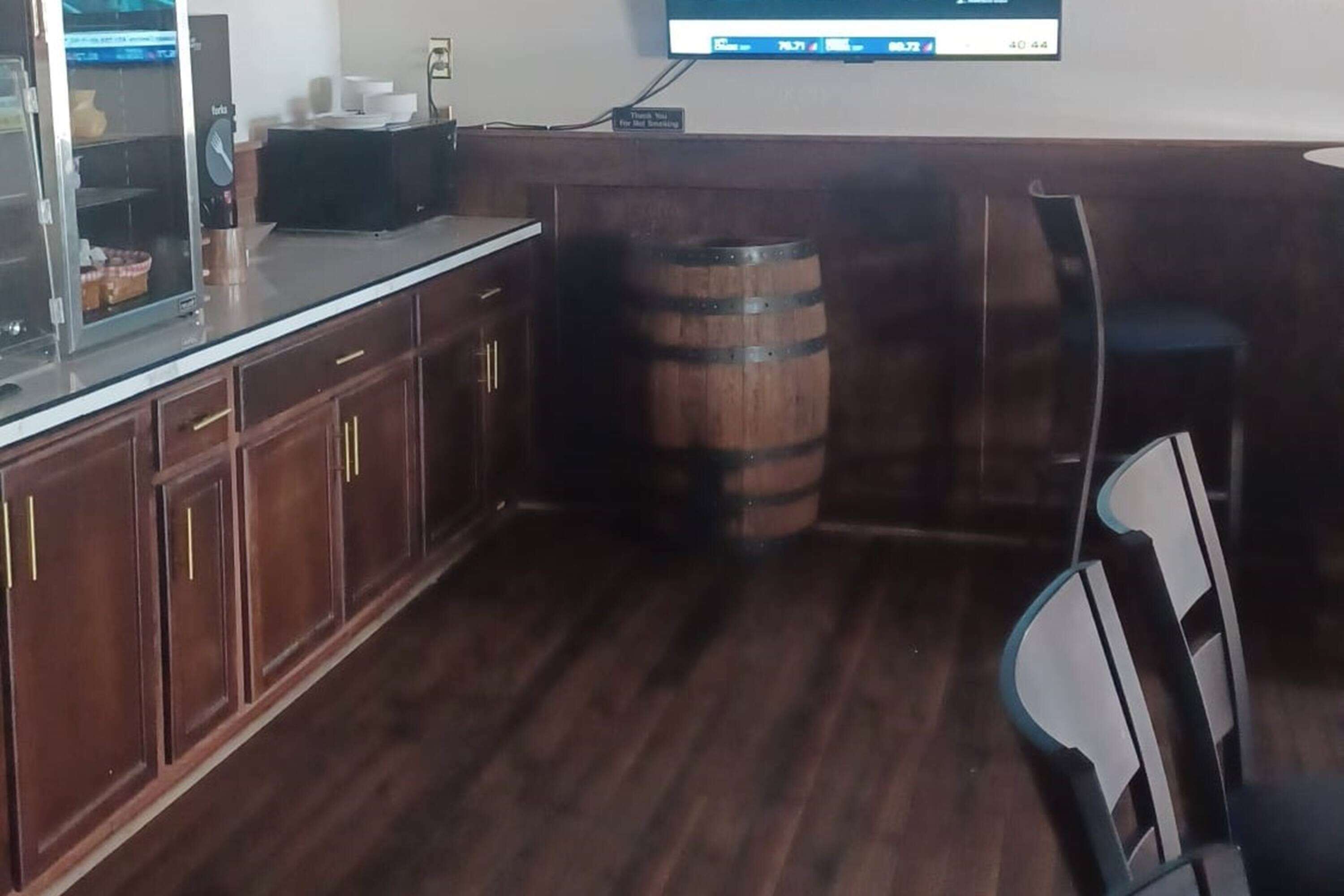 L’intérieur d’un restaurant, avec des meubles de rangement en bois, un comptoir, un tonneau et un téléviseur qui affiche un menu.