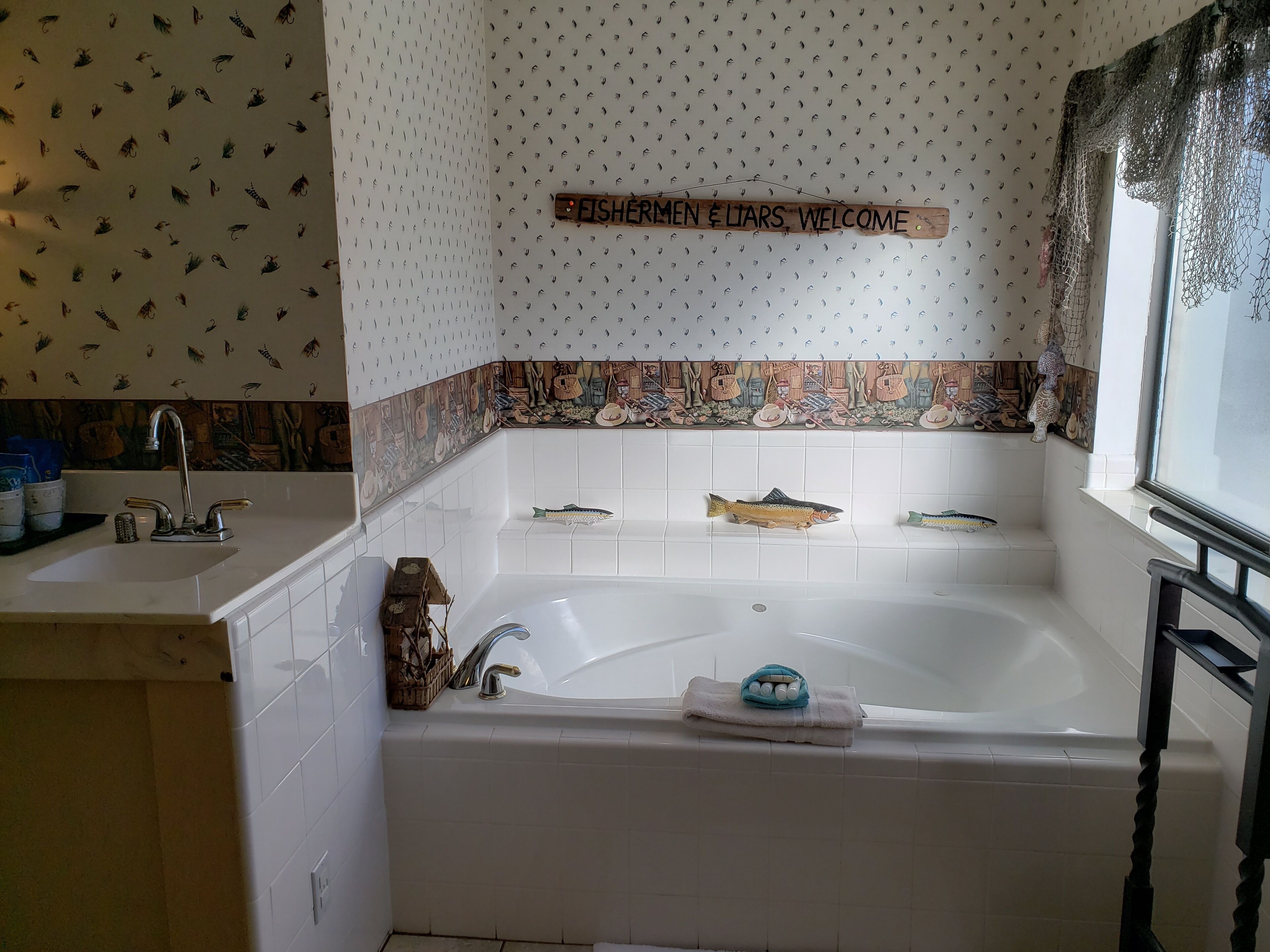 A bathroom with a white bathtub, a sink, and a decorative sign above the tub.