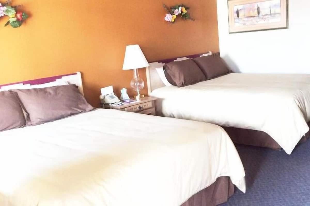 A hotel room with two beds, a nightstand with a lamp, a telephone, and a framed picture on the wall.