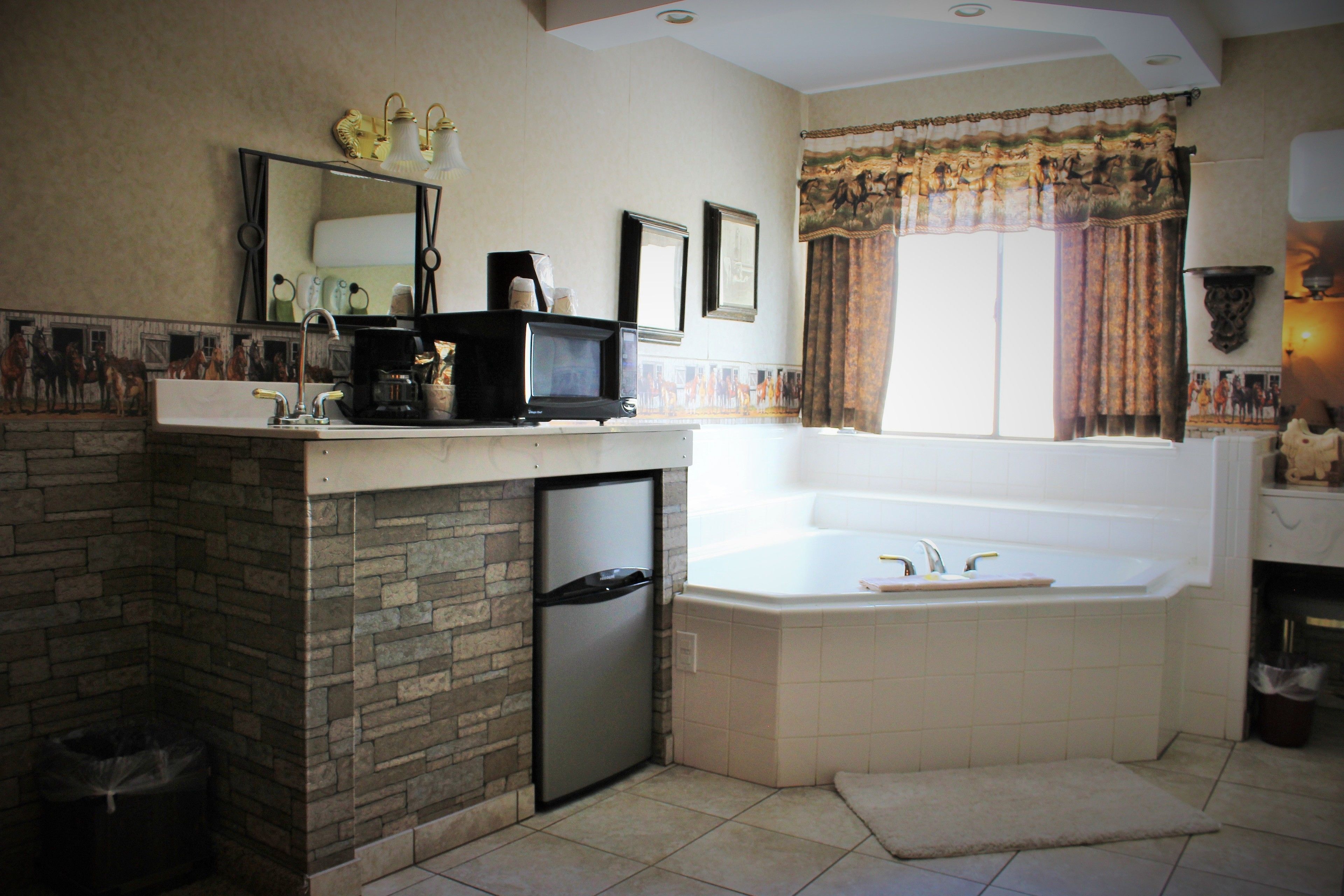 A bathroom with a stone sink, a built-in refrigerator, a large bathtub, and a window with curtains.