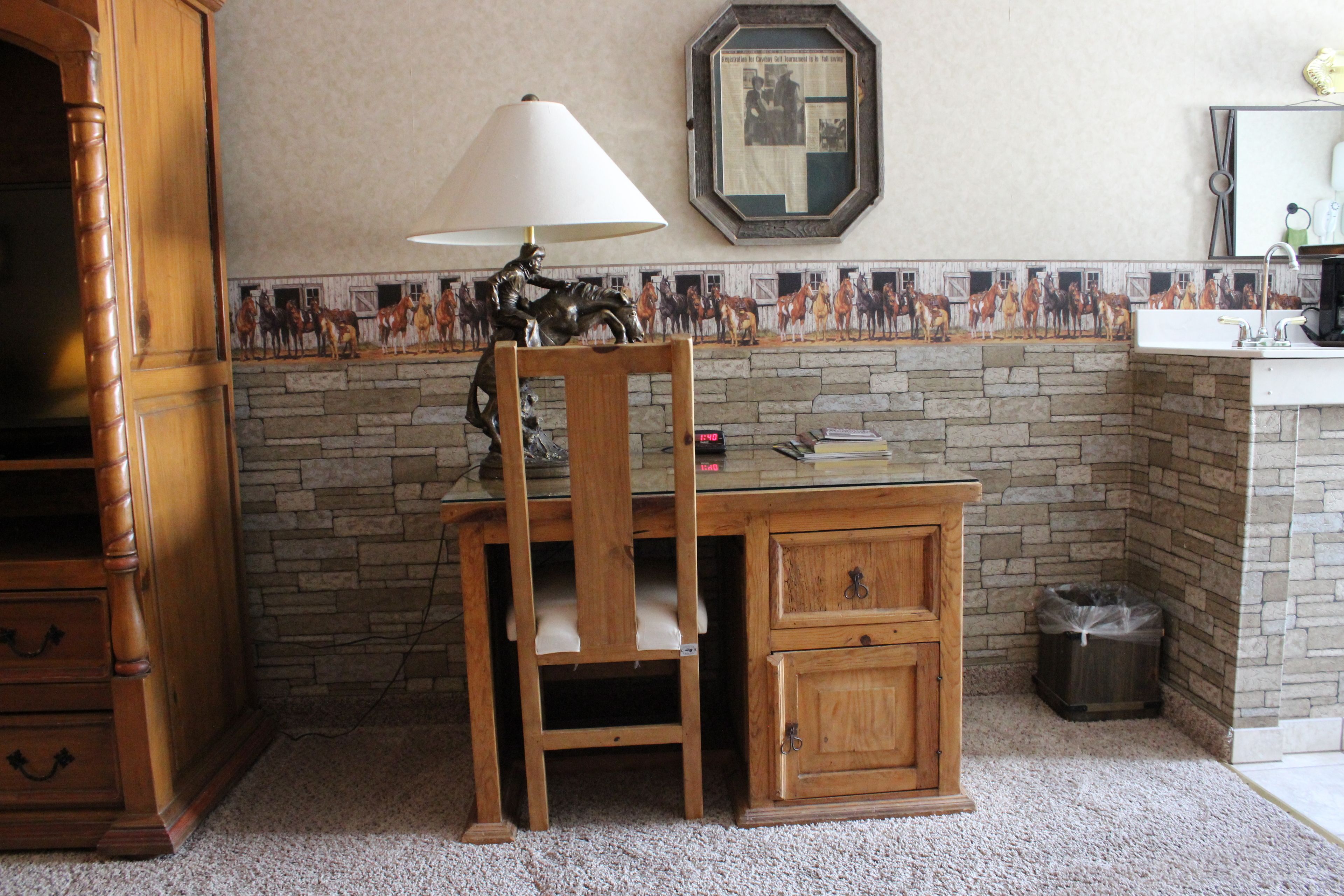 Un petit bureau en bois, une lampe, une chaise, une poubelle et un pare-éclaboussures décoré d’un motif imitant la pierre.
