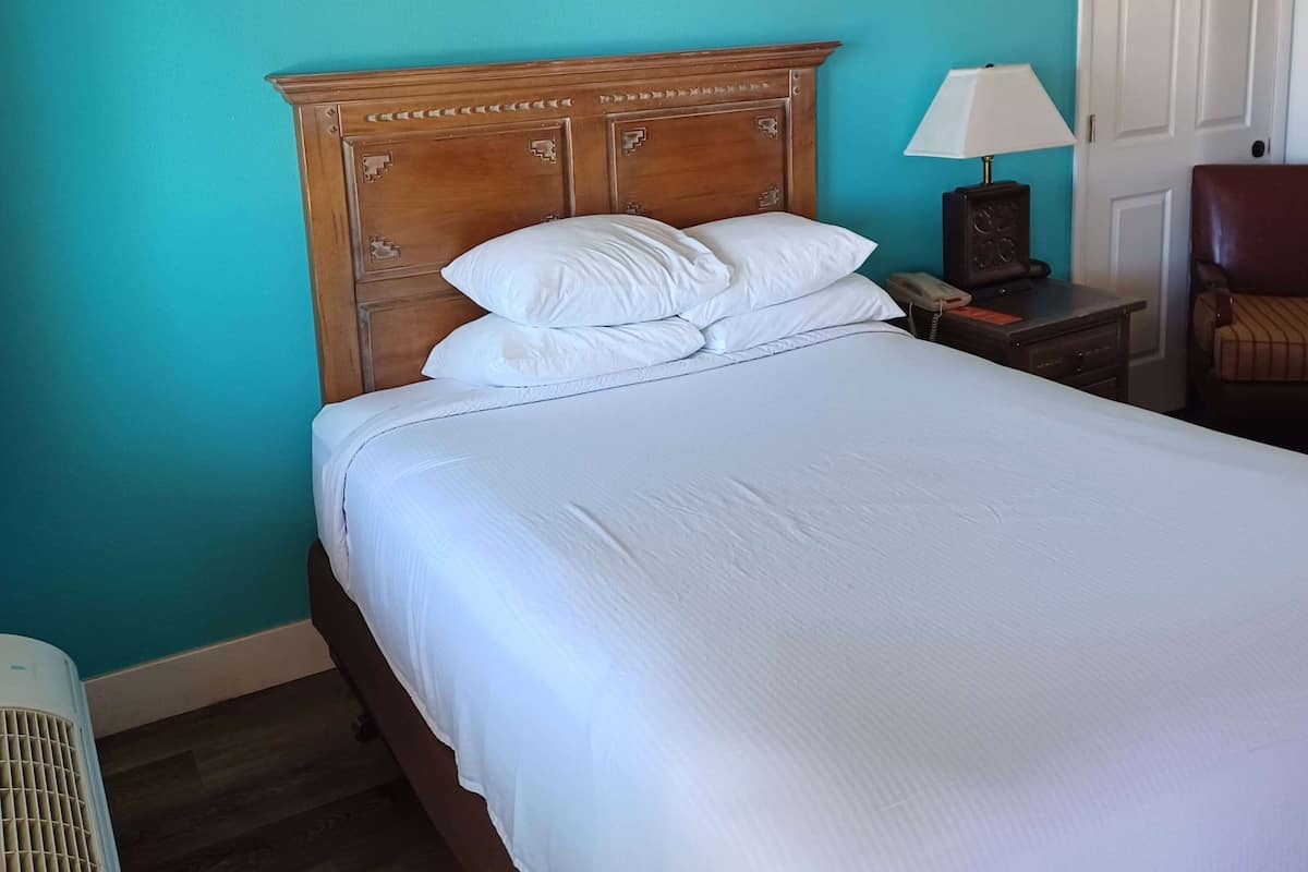 A neatly made bed with white linens, a wooden headboard, a bedside lamp, and a telephone on a nightstand.
