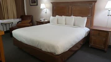 Une chambre d’hôtel avec un grand lit, une tête de lit en bois, une table de chevet avec une lampe, une chaise et un petit bureau.