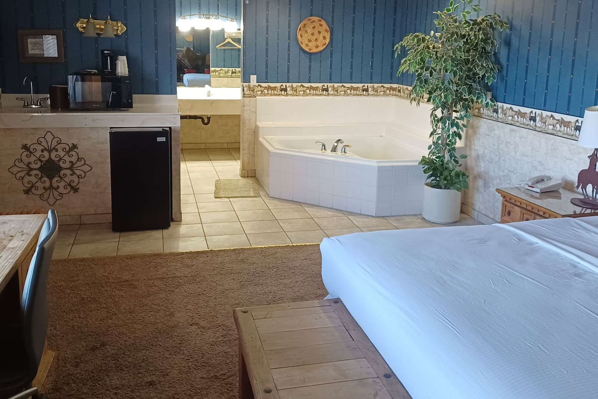 A hotel room with a bed, a small desk with a refrigerator, a sink, and a large bathtub.