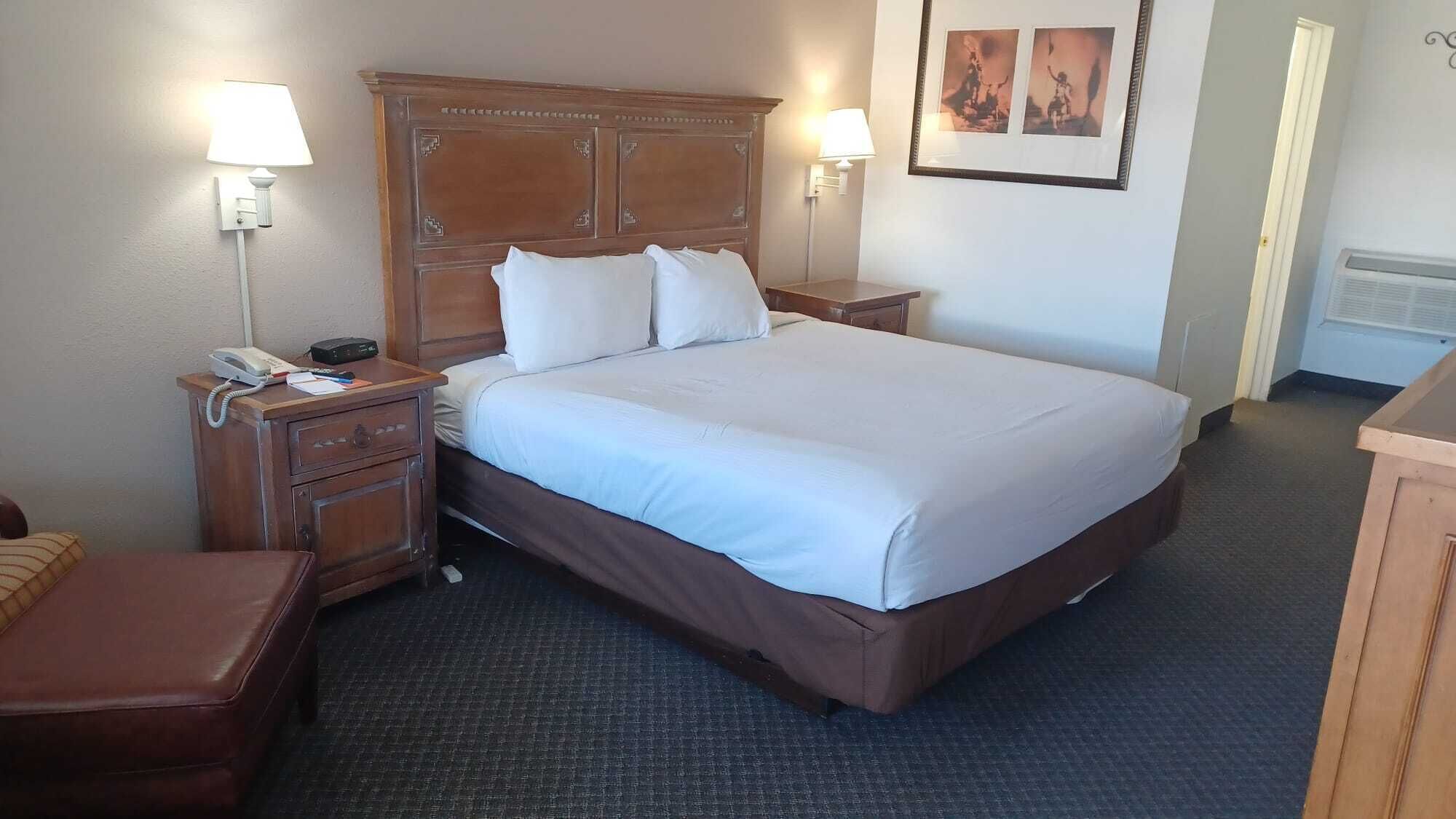 A hotel room with a large bed, two bedside tables with lamps, a telephone, and a small desk with a chair.