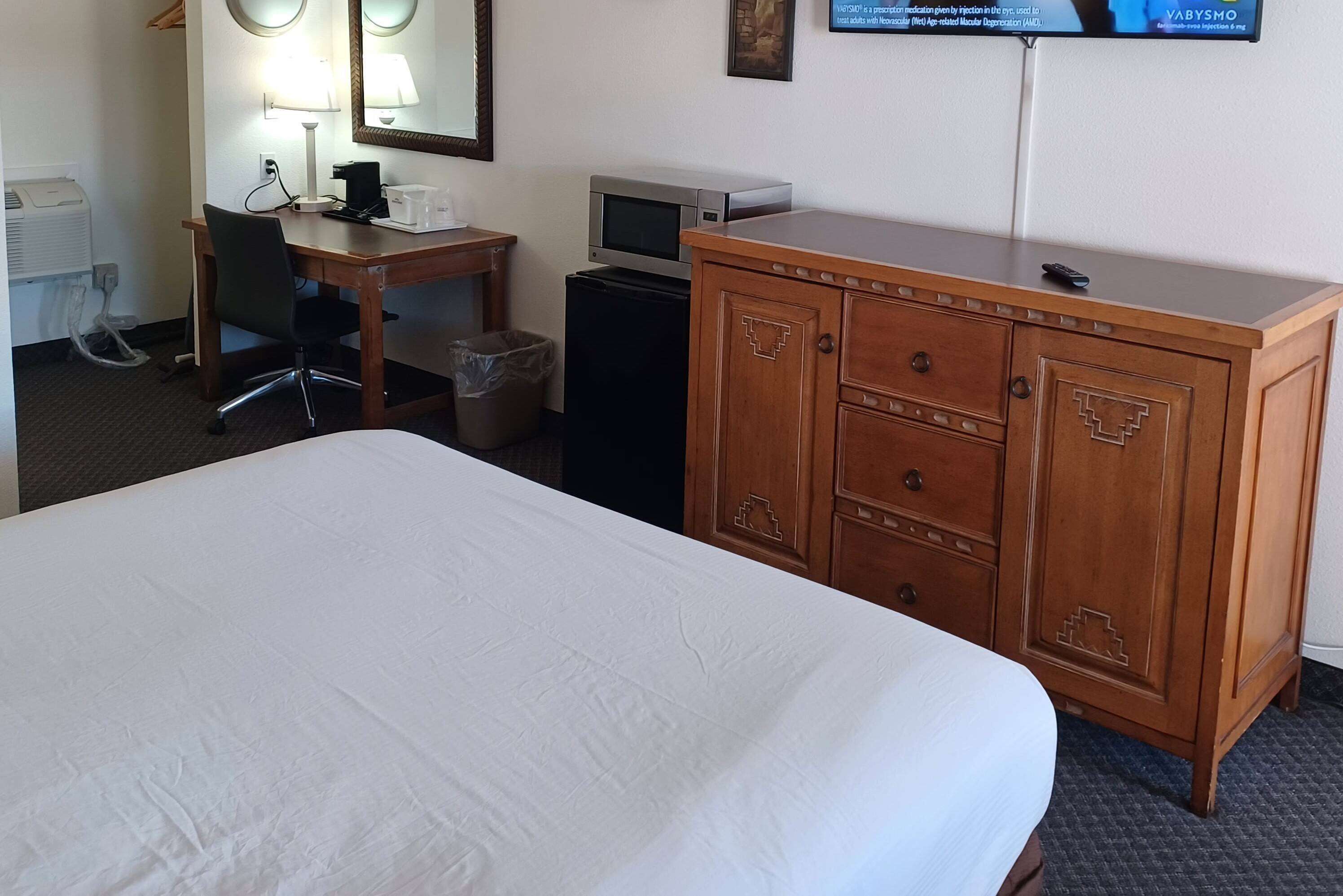 A hotel room with a bed, a desk with a computer, a television, and a wooden dresser.