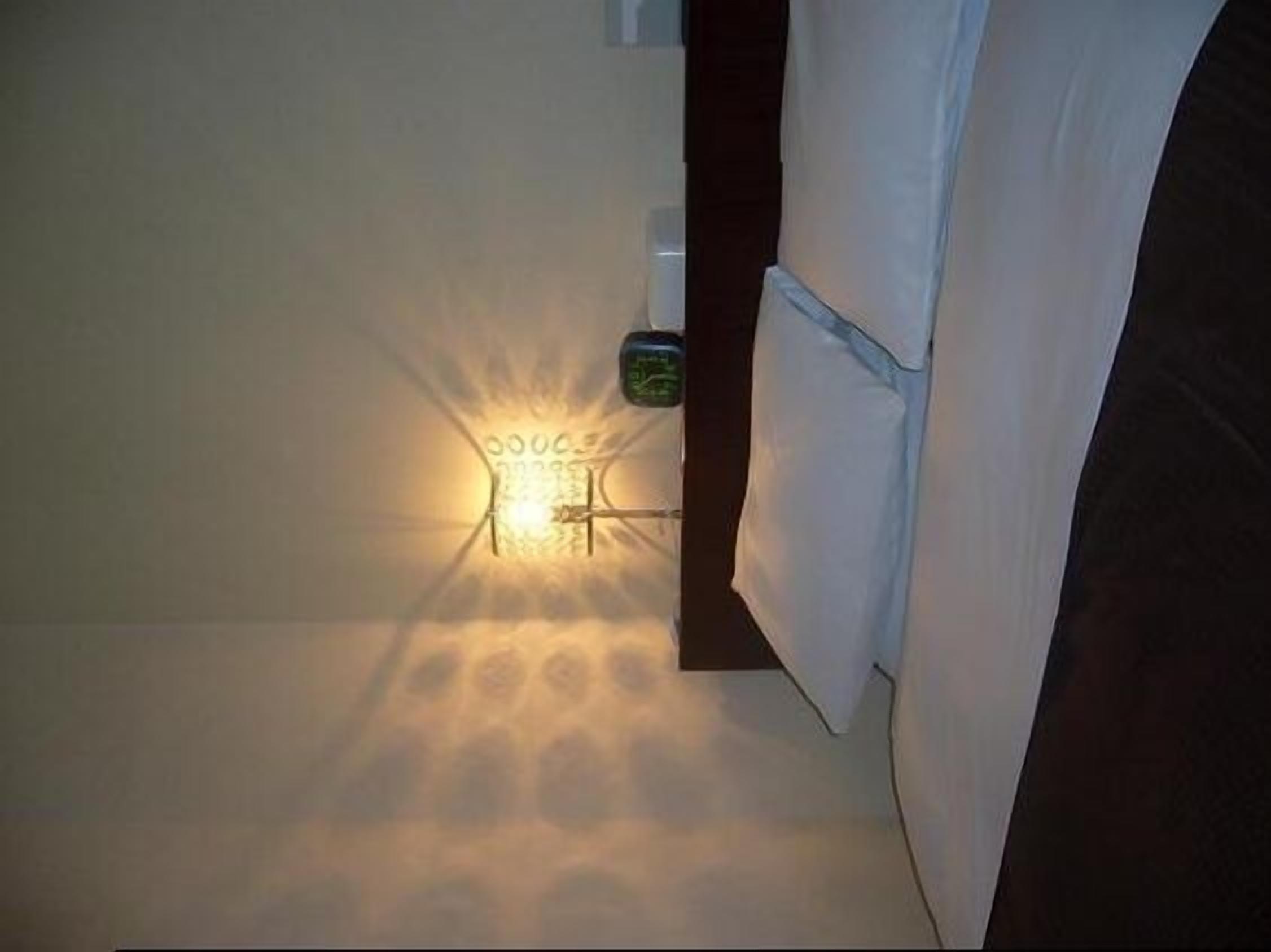 Une pièce comprenant un lit, une table de chevet et un luminaire fixé au mur.