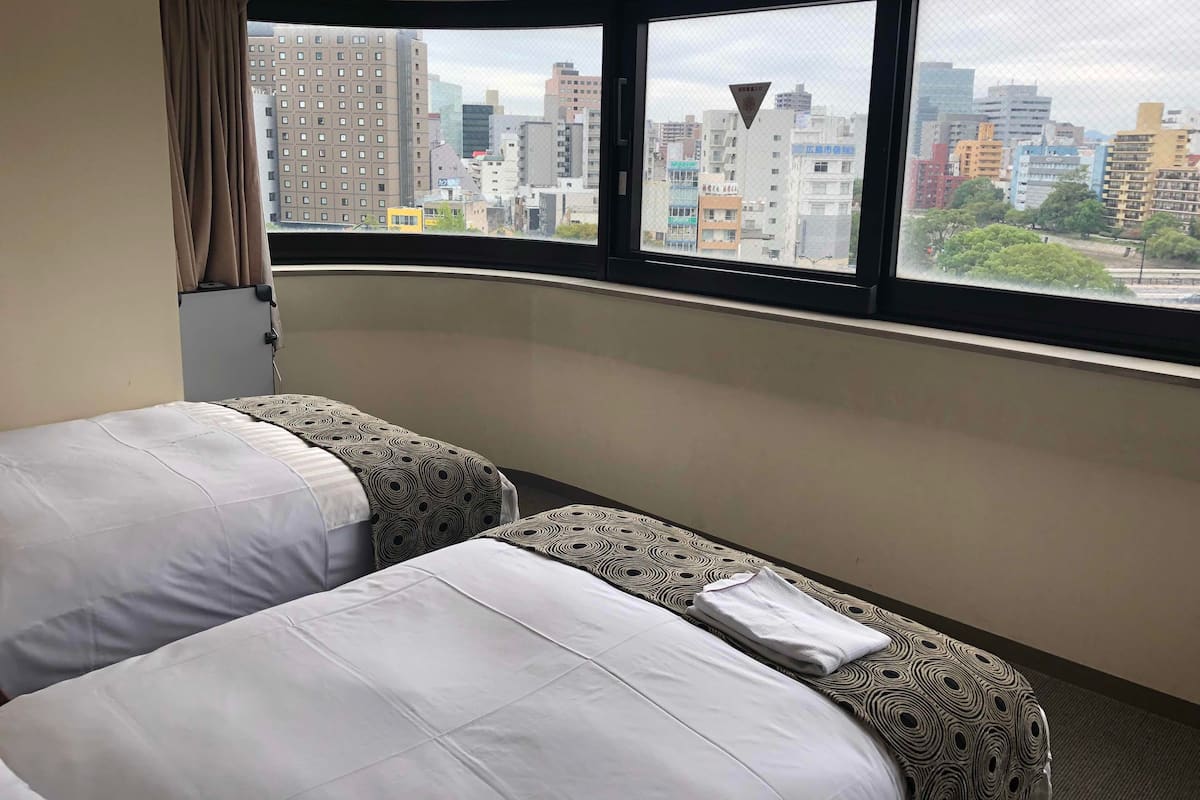 A hotel room with two beds, a large window with a city view, and a curtain.