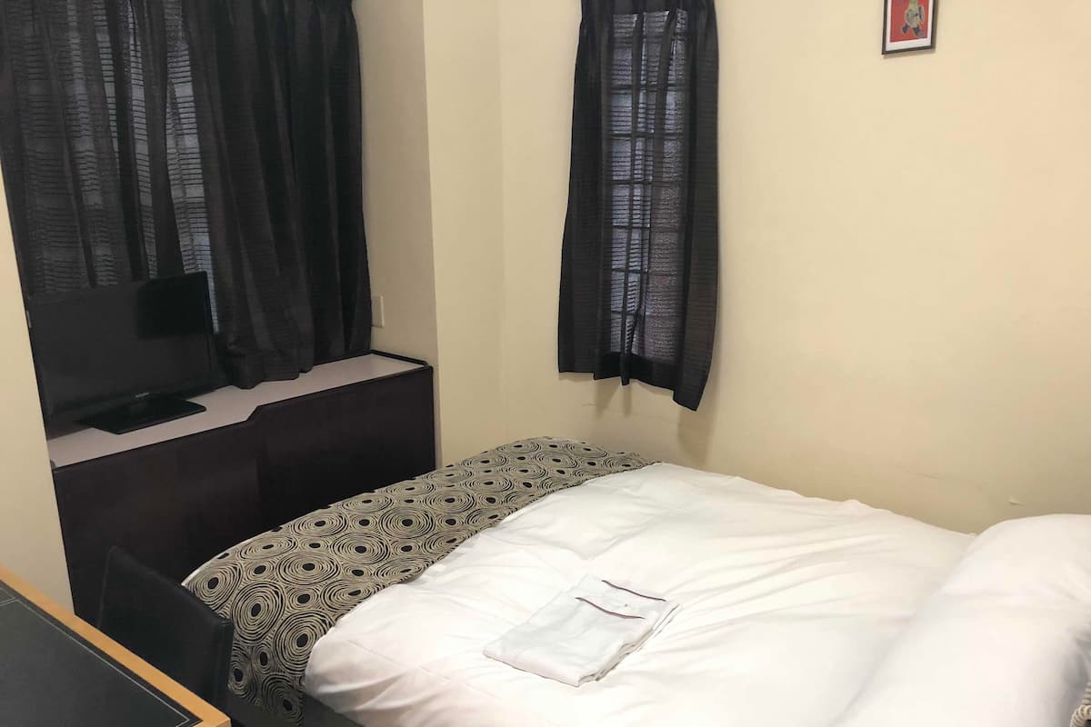 A small, single-bed room with a desk and chair, a TV, and a window with curtains.