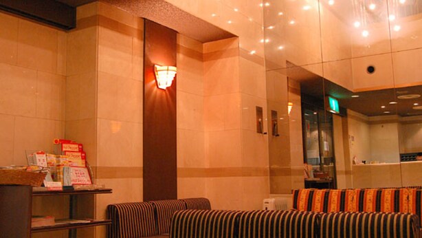 A hotel lobby with a reception desk, a seating area with striped cushions, a large wall-mounted light fixture, and a glass partition. - Hiroshima Ekimae Green Hotel (Hiroshima)