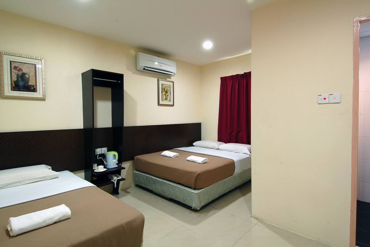 A hotel room with two beds, a bedside table, an air conditioner, and a red curtain.