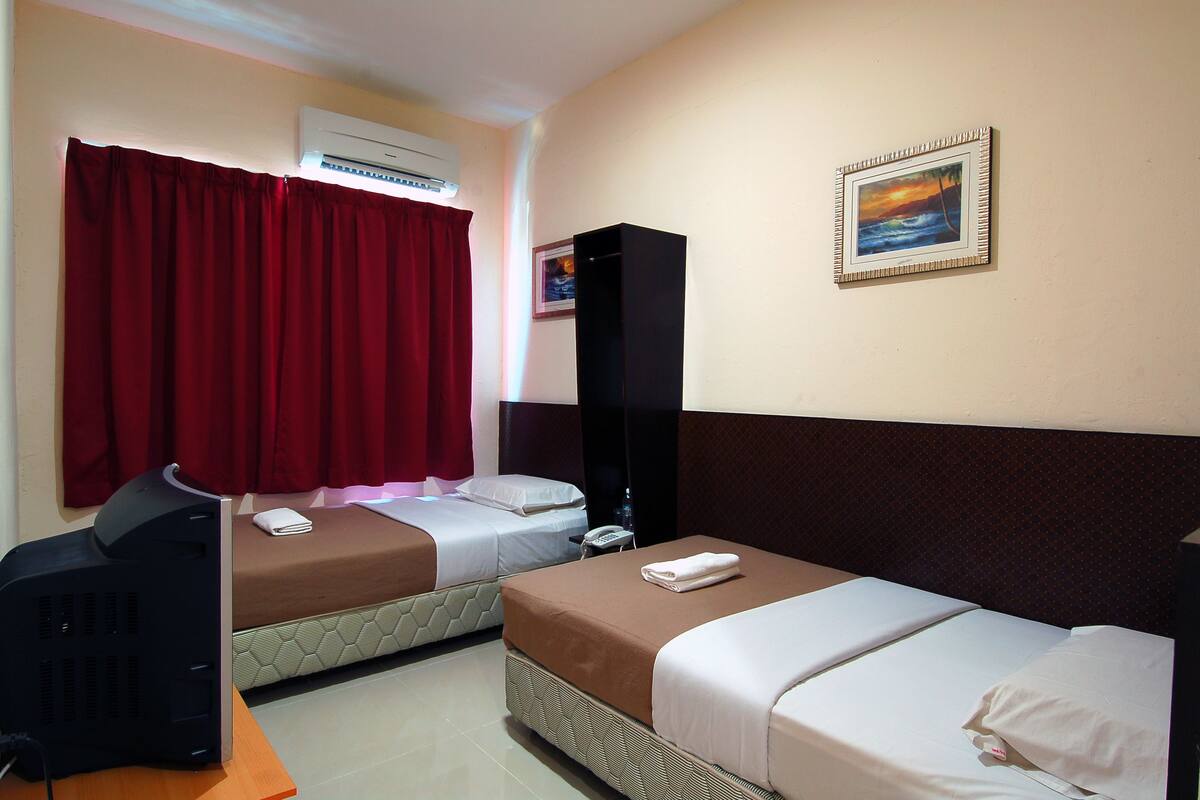 A hotel room with two beds, a TV, an air conditioner, and a painting on the wall.
