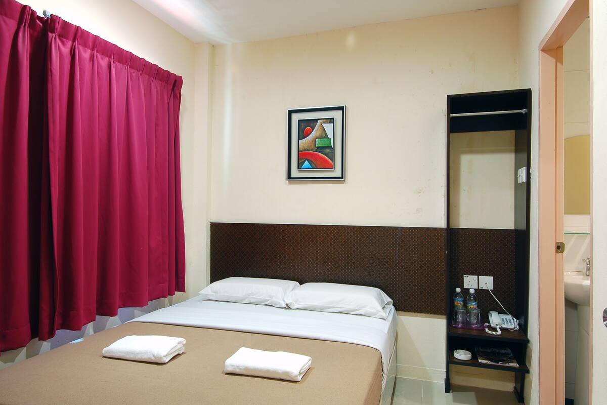 A hotel room with a bed, red curtains, a painting, a mirror, and a small table with toiletries.