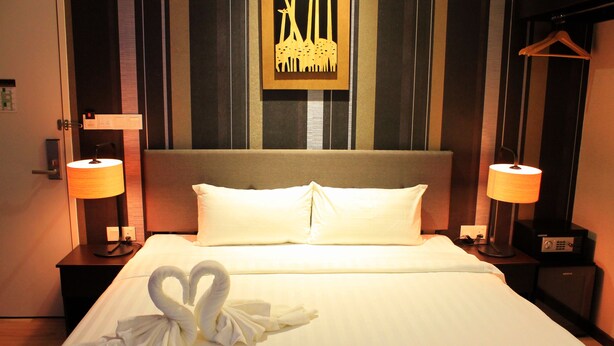A hotel room with a neatly made bed, two bedside lamps, a framed artwork on the wall, and a hanging coat rack.
