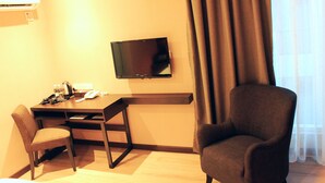 A hotel room with a desk, chair, television, and a large window with curtains.