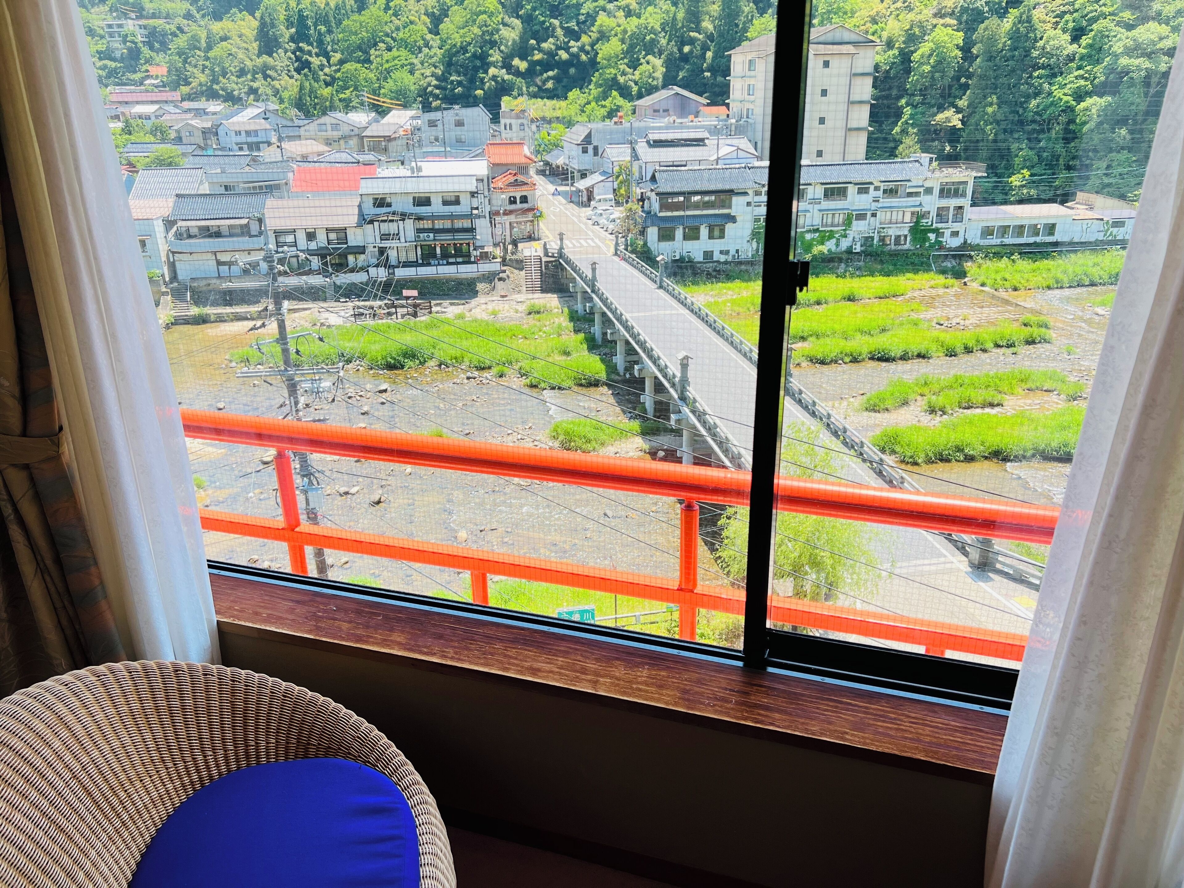 A view from a window overlooking a railway bridge, a residential area with traditional buildings, and a green landscape.