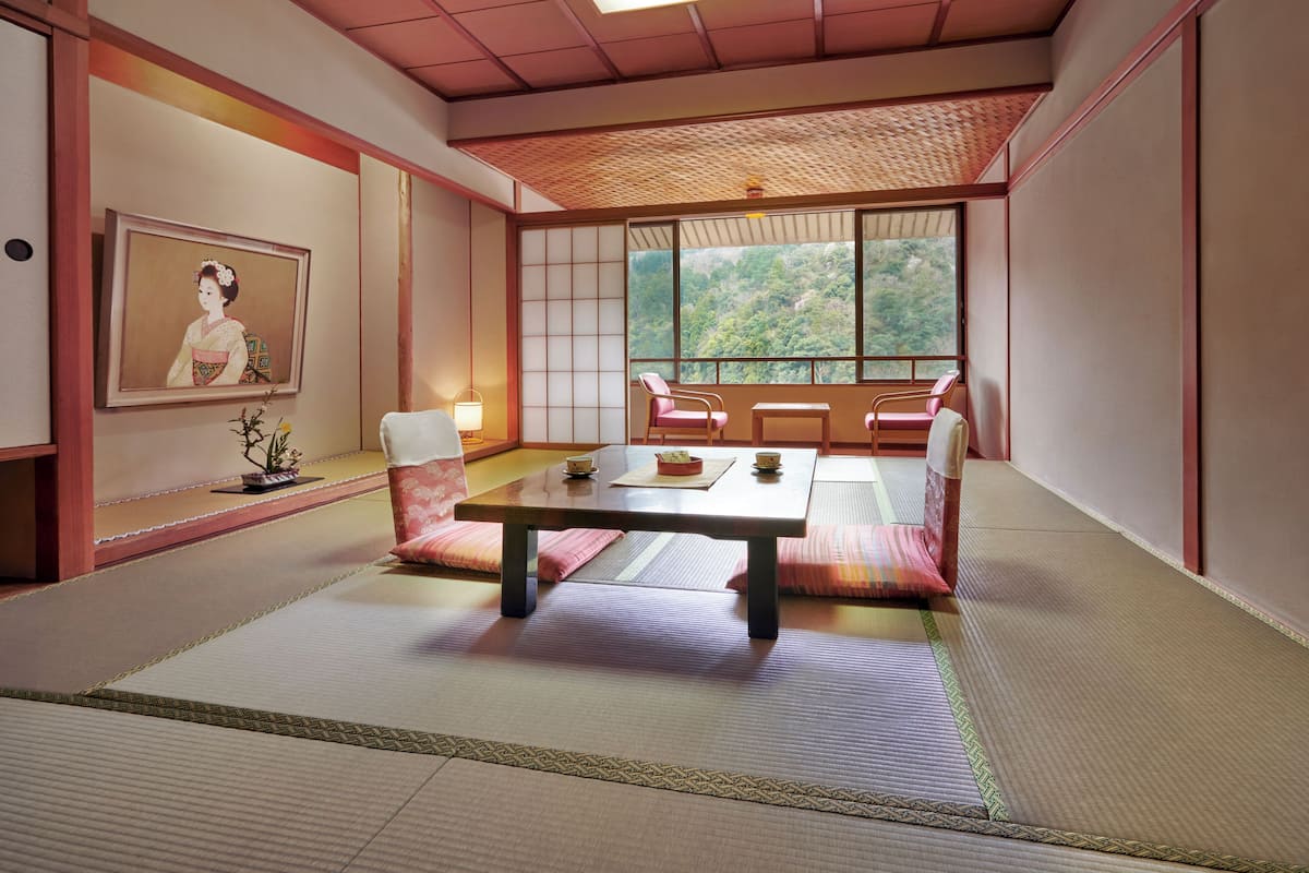 Een traditionele Japanse kamer met tatami vloeren, een lage tafel en uitzicht op een bos door grote ramen.