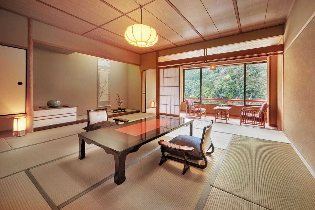 Een traditionele Japanse kamer met tatami vloerbedekking, een lage tafel en uitzicht op een bos door grote ramen.