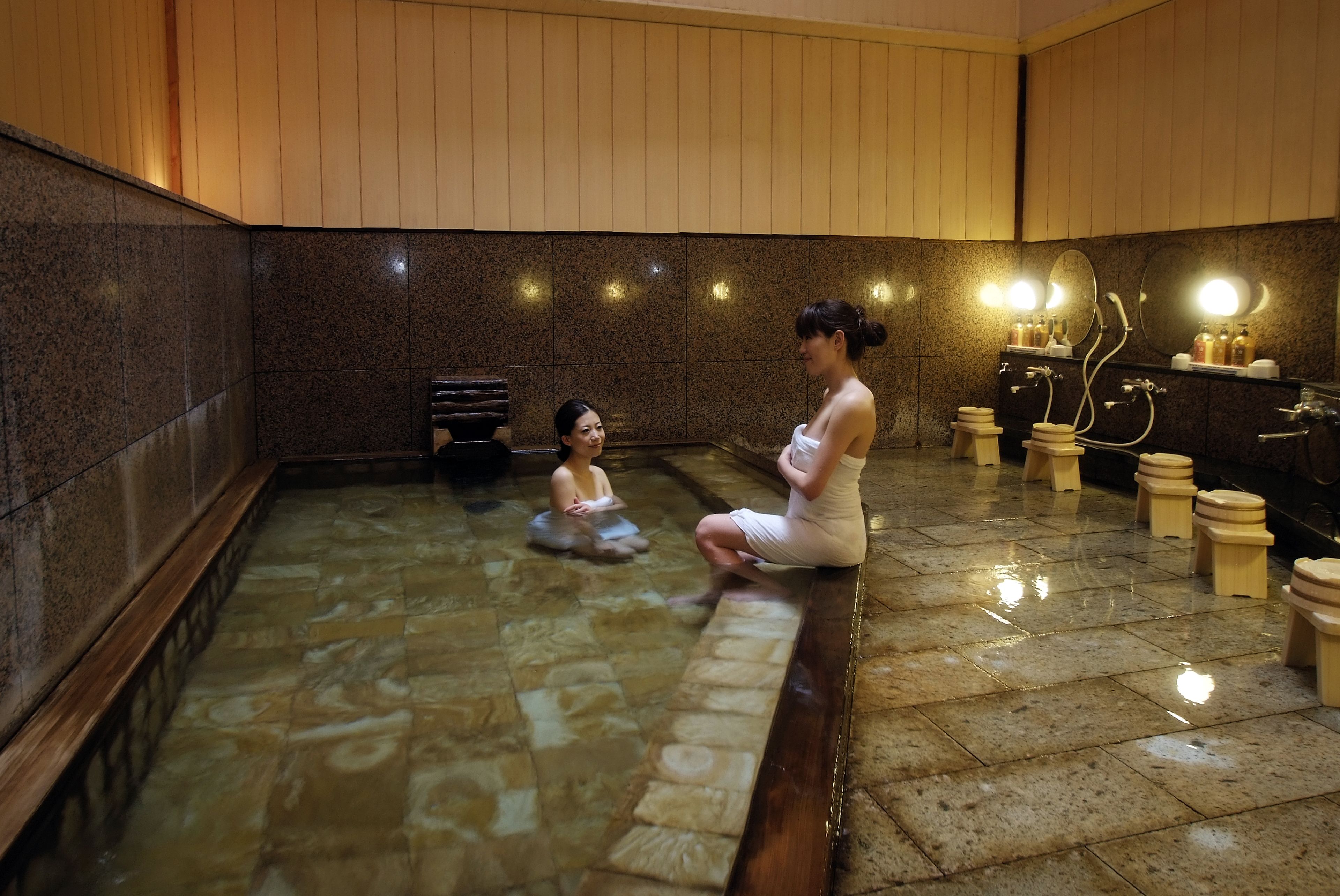 A spa area with a stone floor, wooden benches, and a seating area with a person sitting.