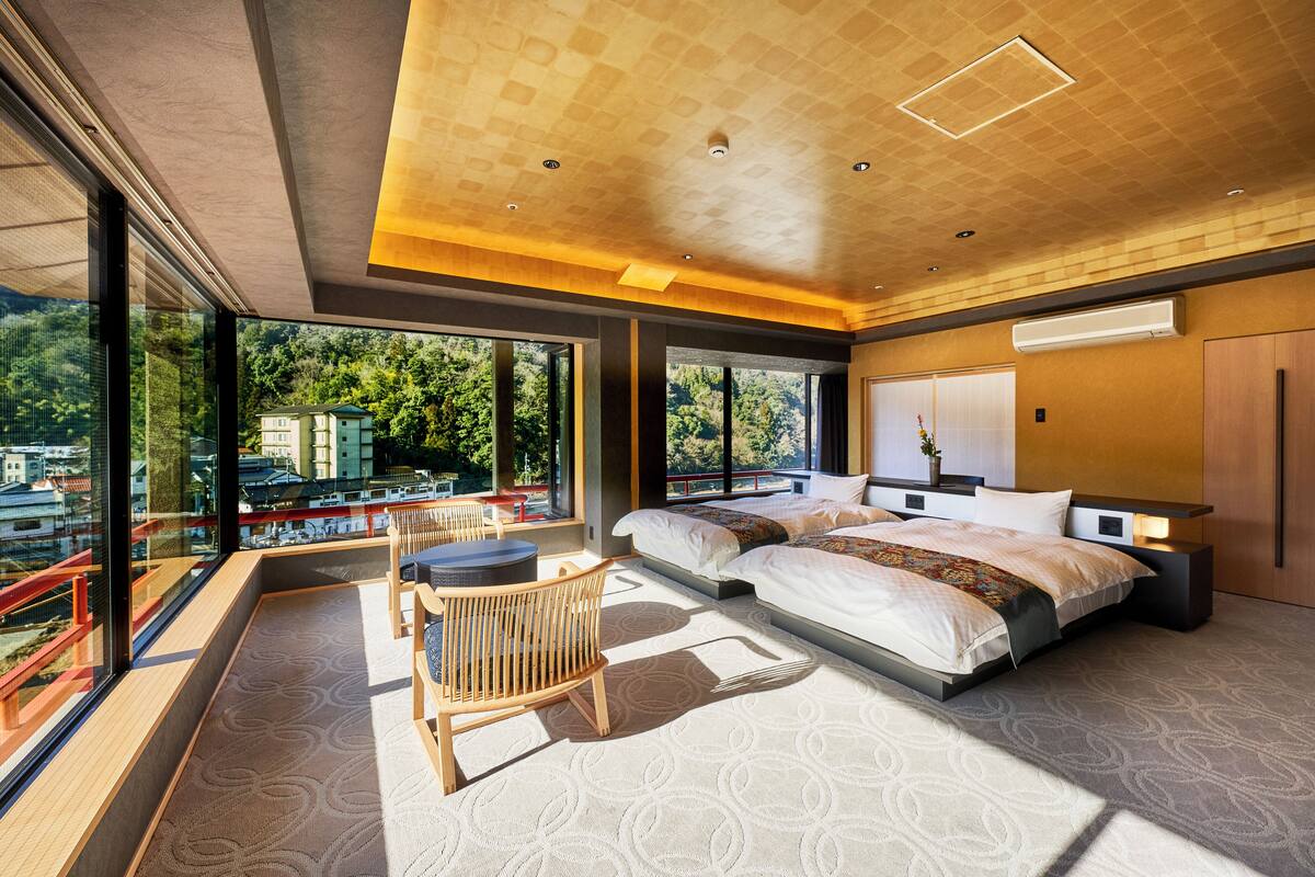 Een moderne slaapkamer met een groot bed, een zithoek met een stoel en uitzicht op de omgeving door grote ramen.