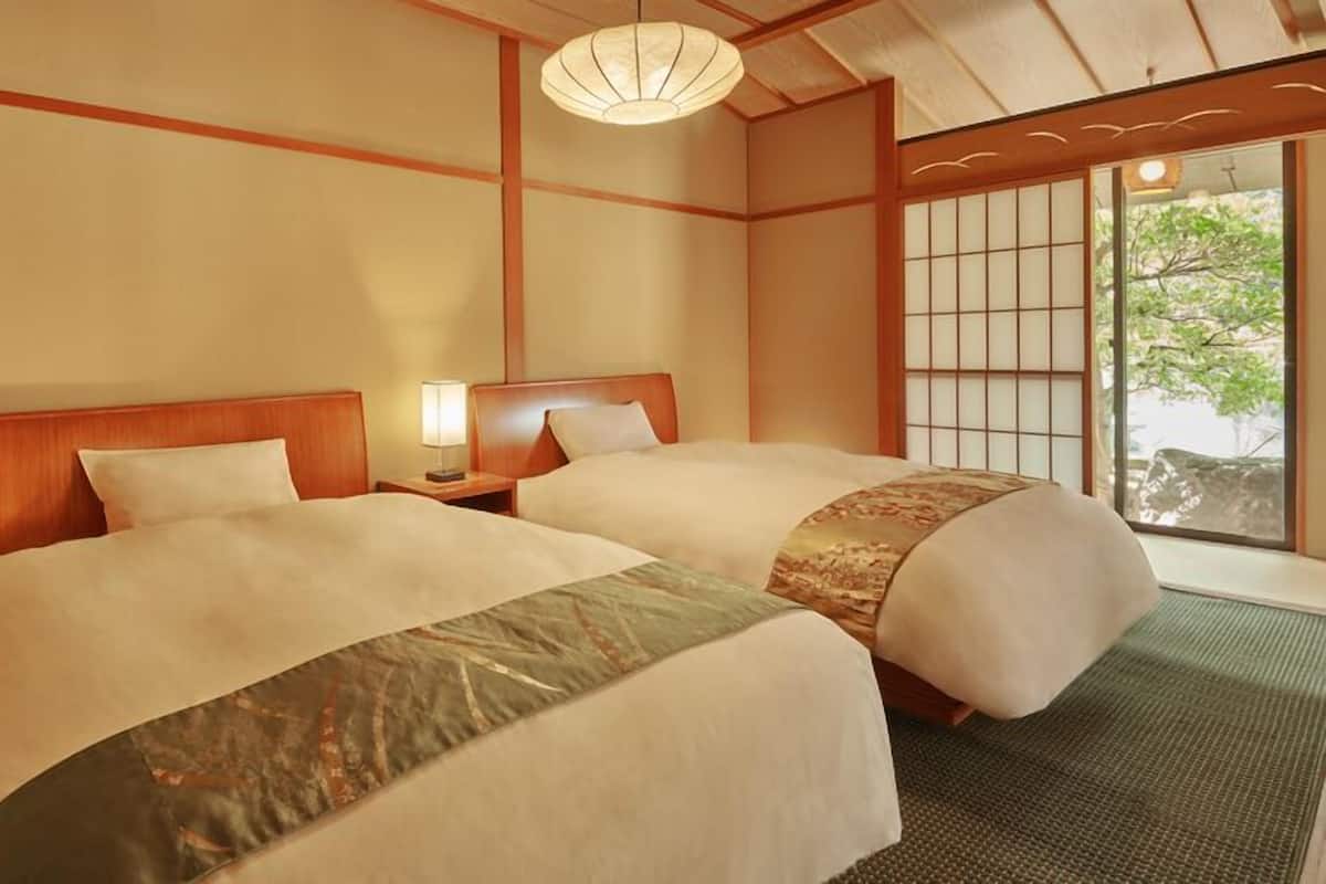 Een traditionele Japanse hotelkamer met tatami vloerbedekking, twee bedden met bijpassende hoofdborden, een shoji scherm en uitzicht op groen buiten.