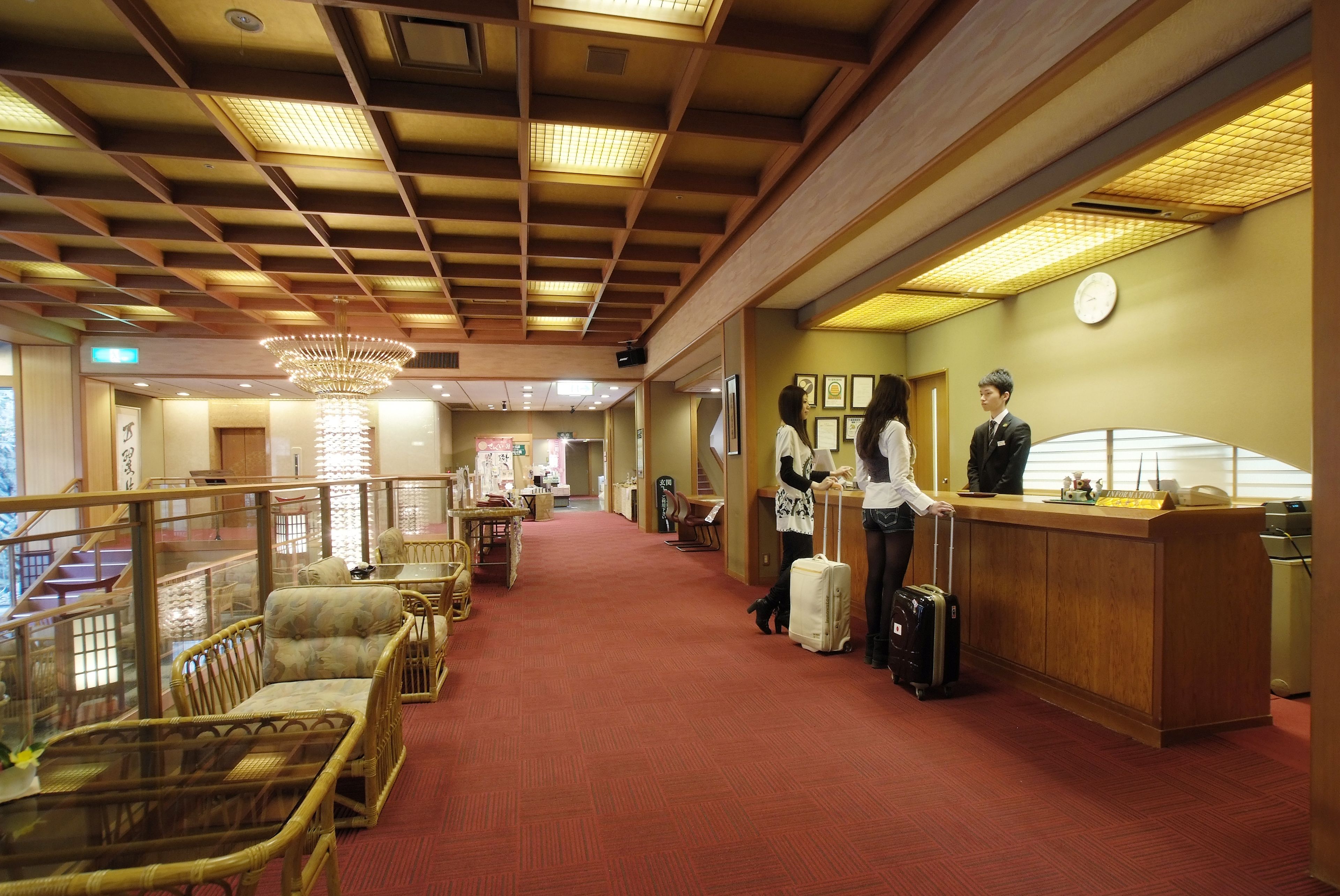 A hotel lobby with a reception desk, seating area, and a staircase leading to an upper level.
