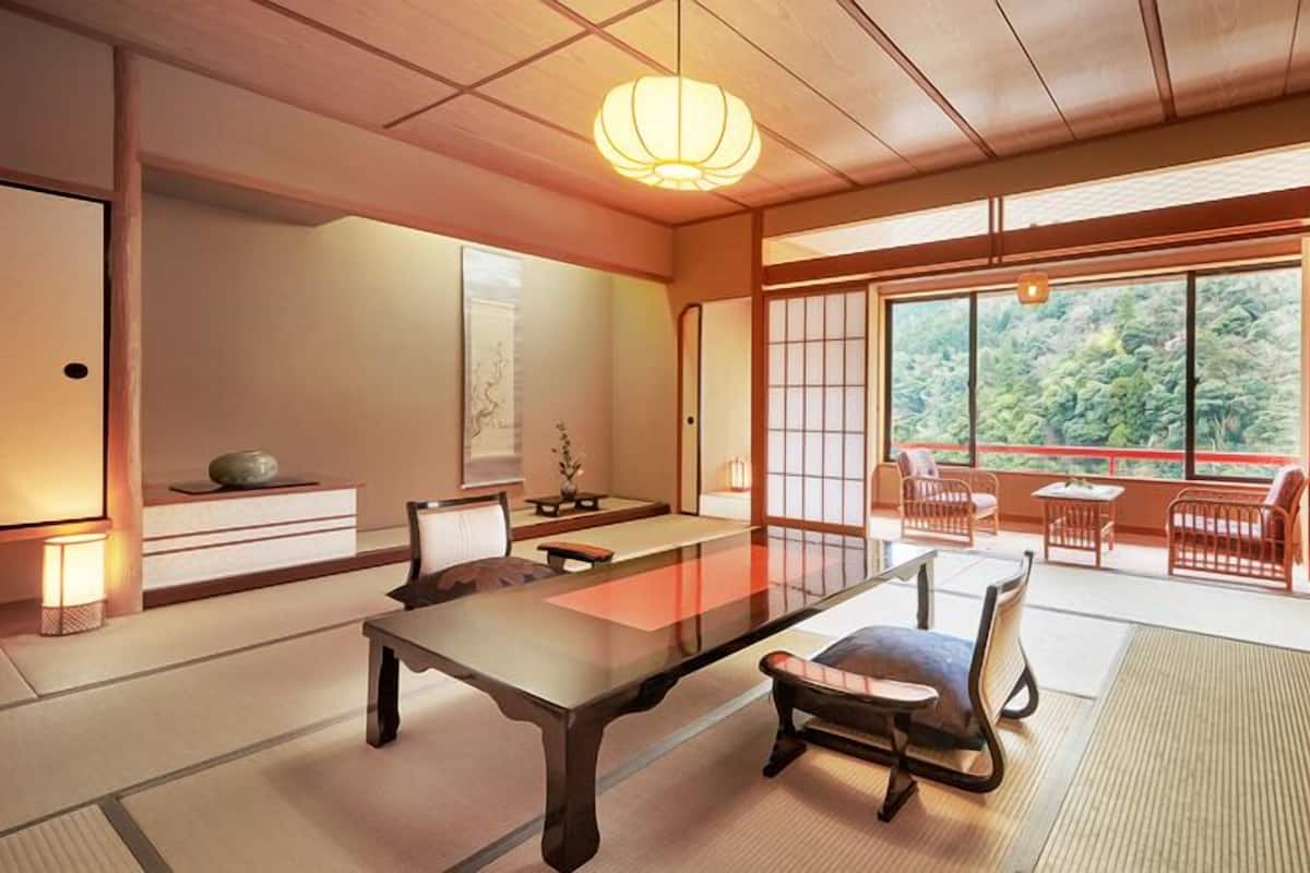 Une pièce de style japonais traditionnel, avec un sol recouvert de tatamis, une table basse et des portes coulissantes donnant sur un balcon offrant une vue sur la verdure.