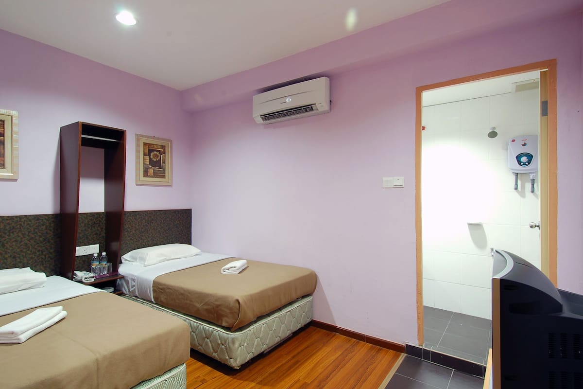 Een hotelkamer met twee bedden, een airco, een douche en een televisie.