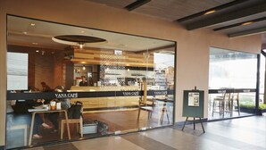 Interior moderno del Vana Café, con escaparate de vidrio, zona de estar y cartelera de menú visible.