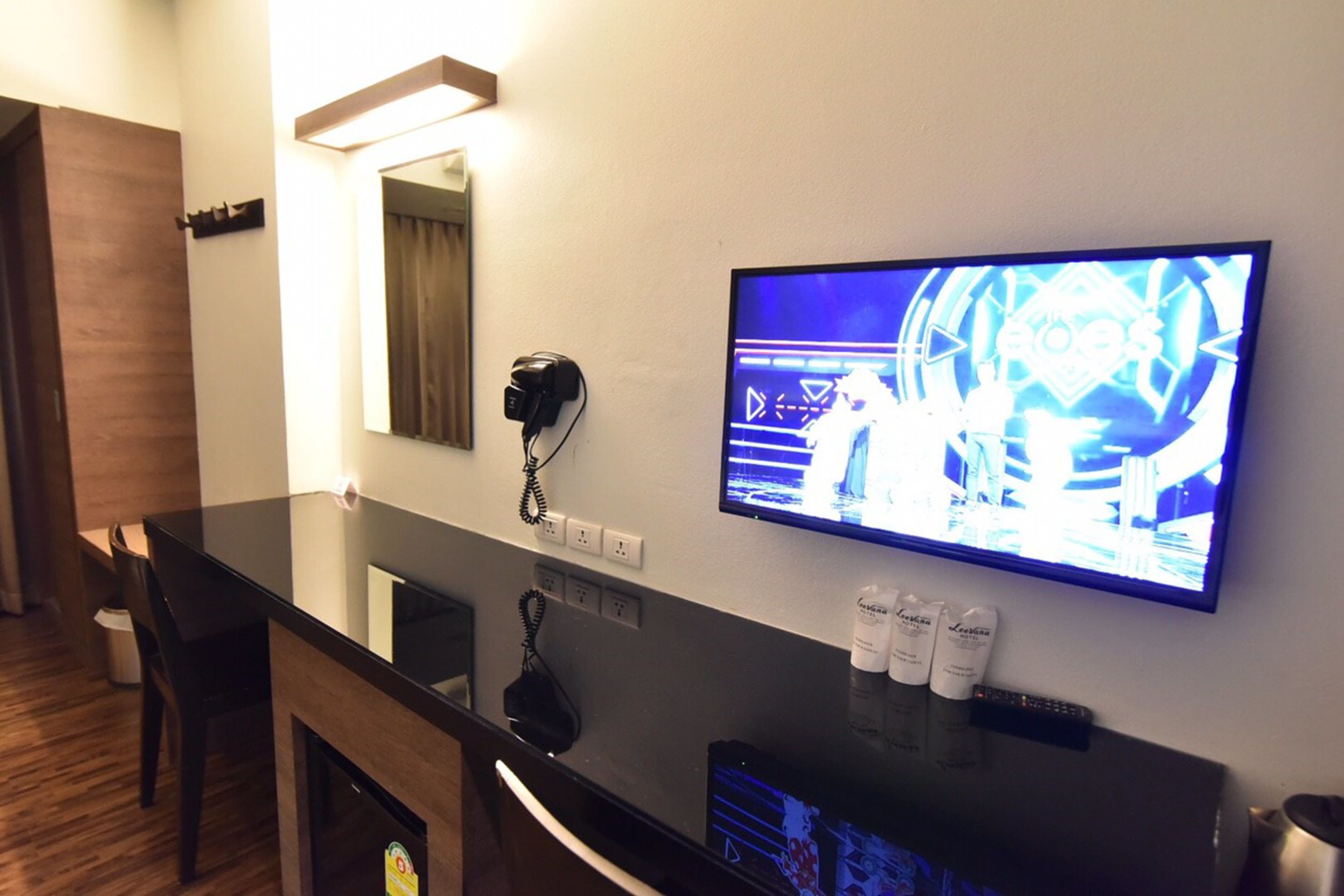 Habitació d'hotel amb un taulell de recepció negre, una televisió penjada, un telèfon i un mirall.