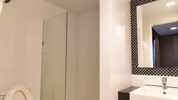 Un baño moderno con inodoro, cabina de ducha de vidrio, lavabo y espejo con marco a cuadros.