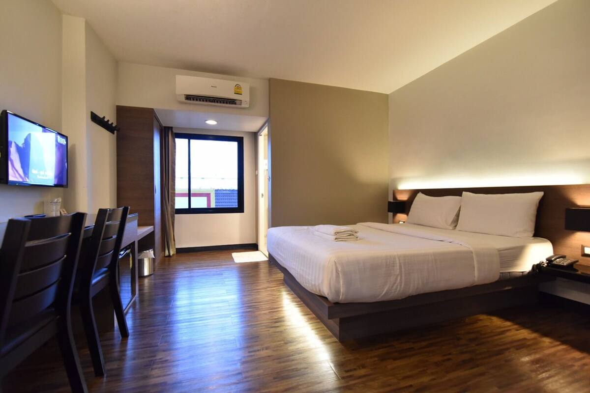 Habitación de hotel con cama, mesita de noche, televisión y vistas al exterior.