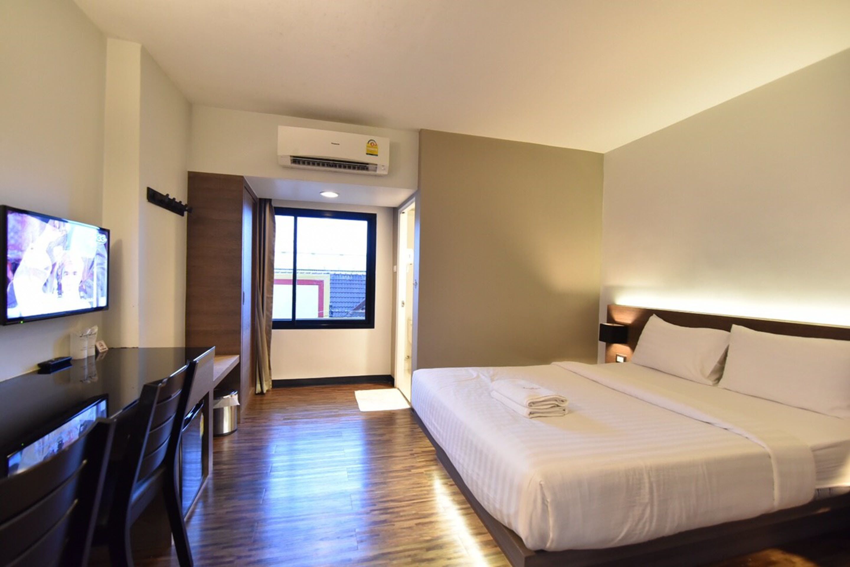 A hotel room with a bed, a desk, a television, and an air conditioning unit.