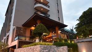 Un hotel moderno con fachada de piedra, varios balcones y un jardín bien cuidado.