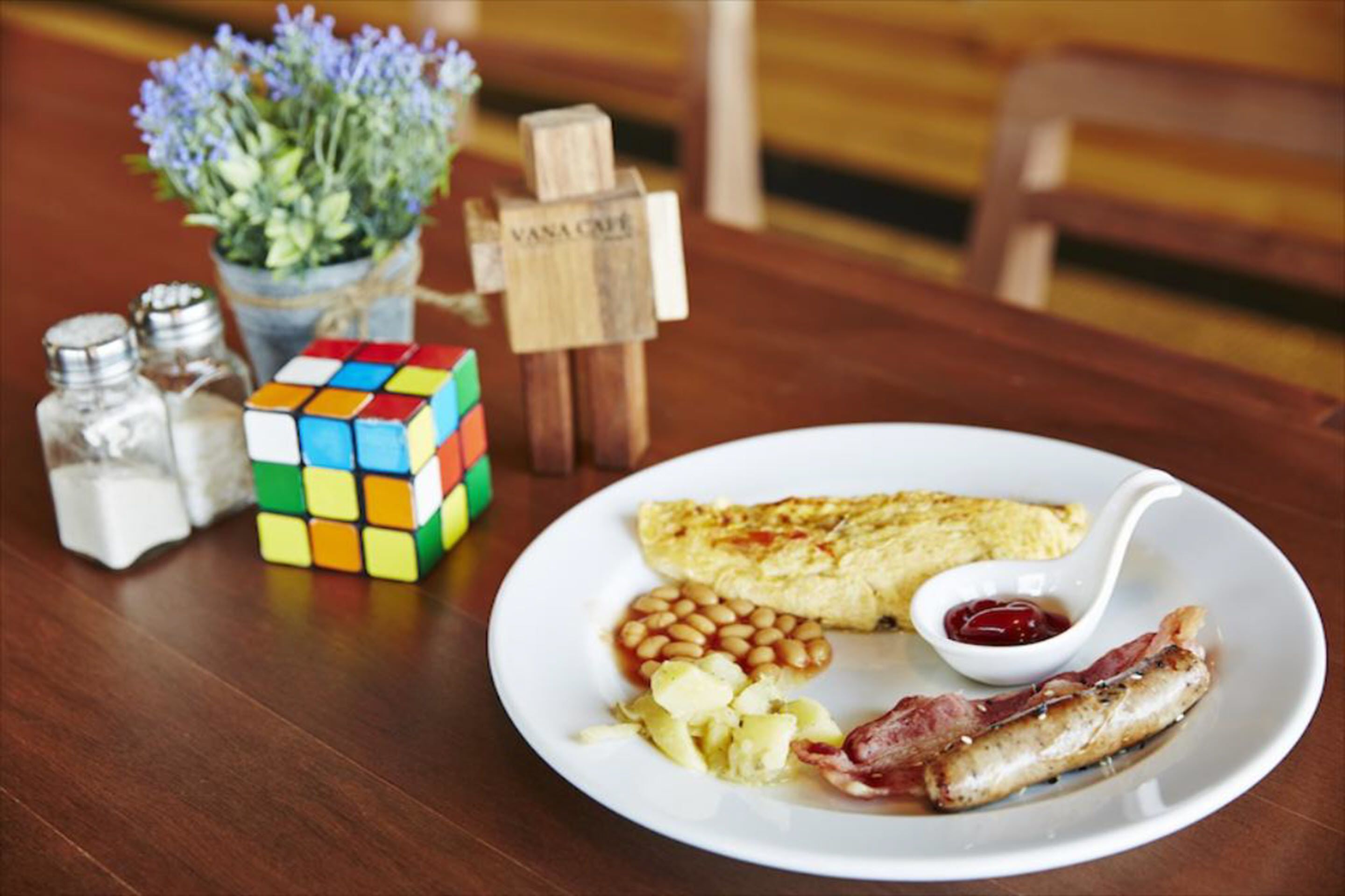 A plate of food with beans, potatoes, bacon, and a scrambled egg on a white plate.