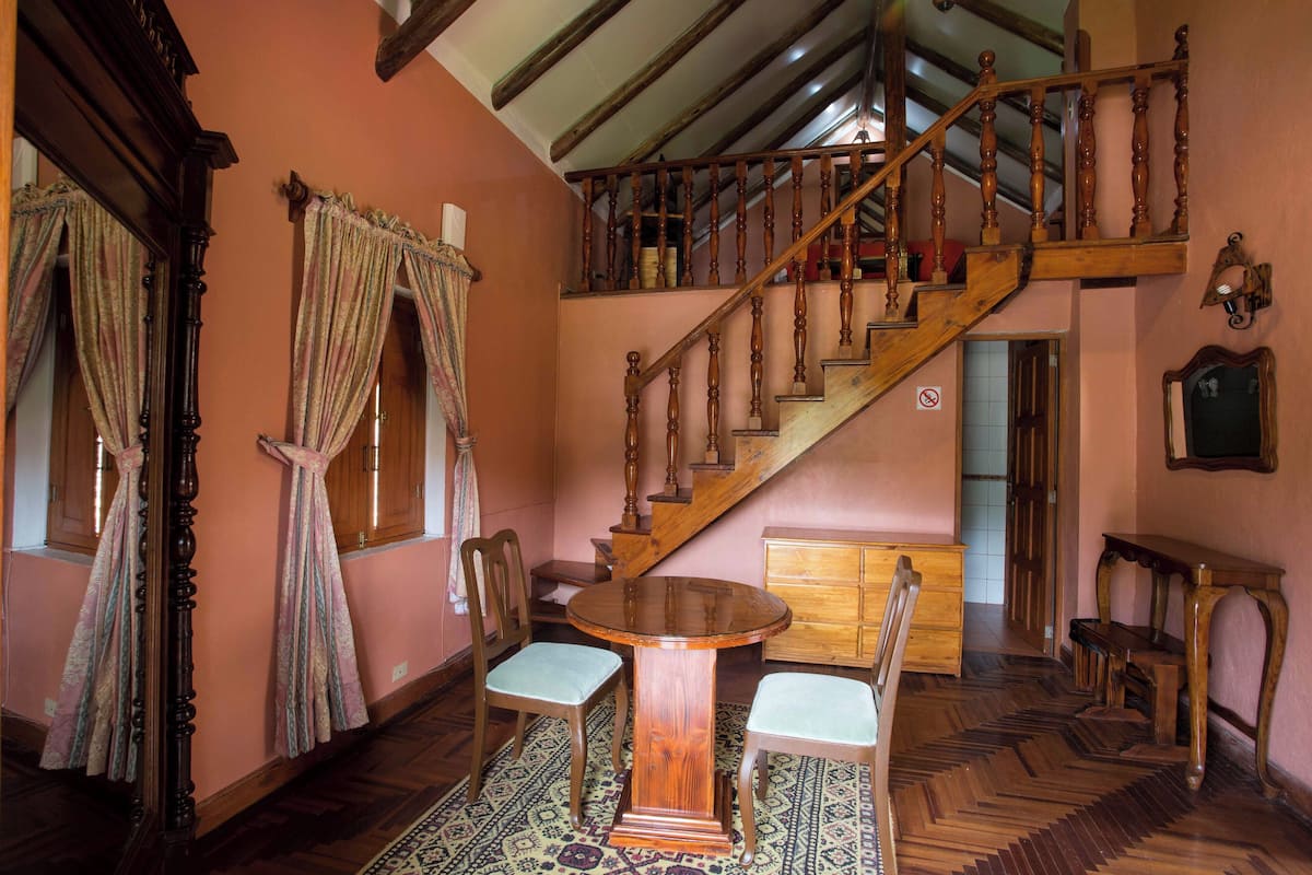 Una habitación tradicional con una escalera de madera, una mesa redonda de madera y sillas, y una alfombra estampada.